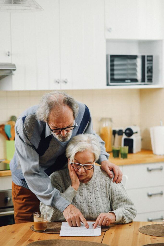 Elderly couple reviewing documents together at the kitchen table, focusing on financial plans.